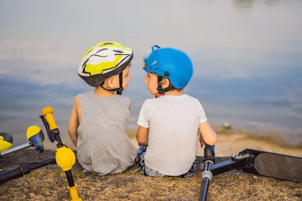 İki erkek bir bisiklet ve scooter sürdükten sonra göl kıyısında oturup — Stok fotoğraf