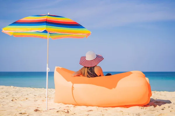 Retrato de estilo de vida de verano de una chica bonita sentada en el sofá inflable naranja en la playa de la isla tropical. Relajarse y disfrutar de la vida en la cama de aire — Foto de Stock