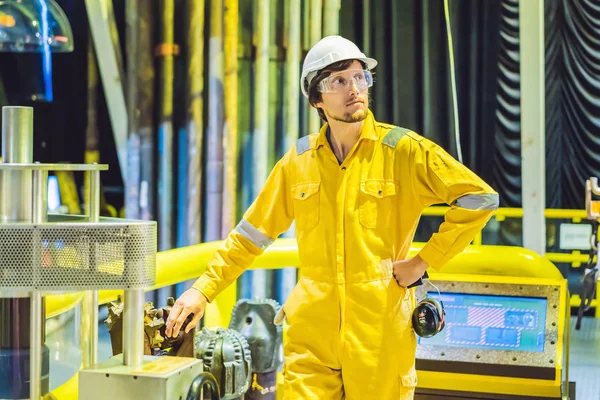 Joven en uniforme de trabajo amarillo, gafas y casco en ambiente industrial, plataforma petrolera o planta de gas licuado — Foto de Stock