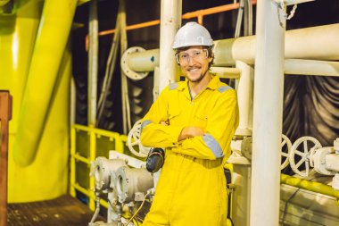 Young man in a yellow work uniform, glasses and helmet in industrial environment,oil Platform or liquefied gas plant