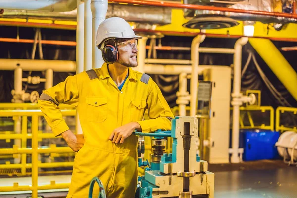 Joven en uniforme de trabajo amarillo, gafas y casco en ambiente industrial, plataforma petrolera o planta de gas licuado — Foto de Stock