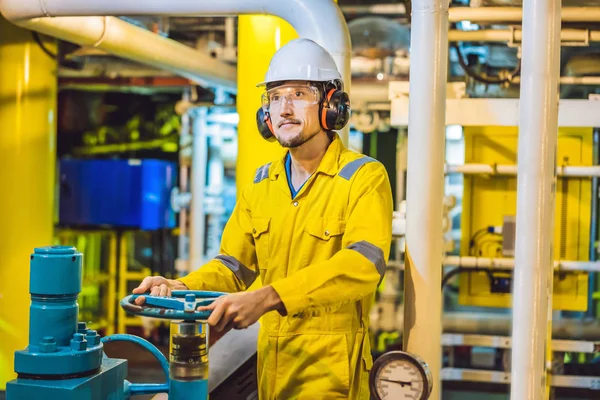 Giovane in uniforme da lavoro gialla, occhiali e casco in ambiente industriale, piattaforma petrolifera o impianto a gas liquefatto — Foto Stock