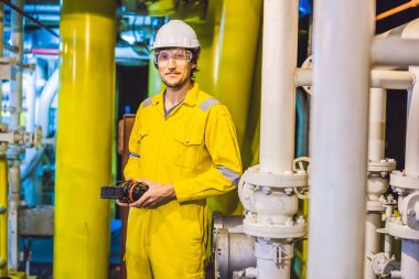 Young man in a yellow work uniform, glasses and helmet in industrial environment,oil Platform or liquefied gas plant
