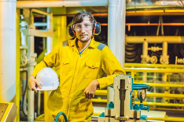 Giovane in uniforme da lavoro gialla, occhiali e casco in ambiente industriale, piattaforma petrolifera o impianto a gas liquefatto — Foto Stock