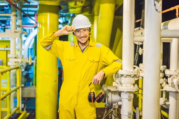 Giovane in uniforme da lavoro gialla, occhiali e casco in ambiente industriale, piattaforma petrolifera o impianto a gas liquefatto — Foto Stock