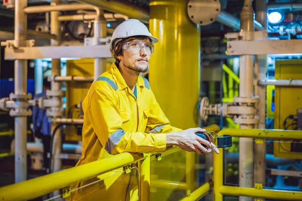 Giovane in uniforme da lavoro gialla, occhiali e casco in ambiente industriale, piattaforma petrolifera o impianto a gas liquefatto — Foto Stock