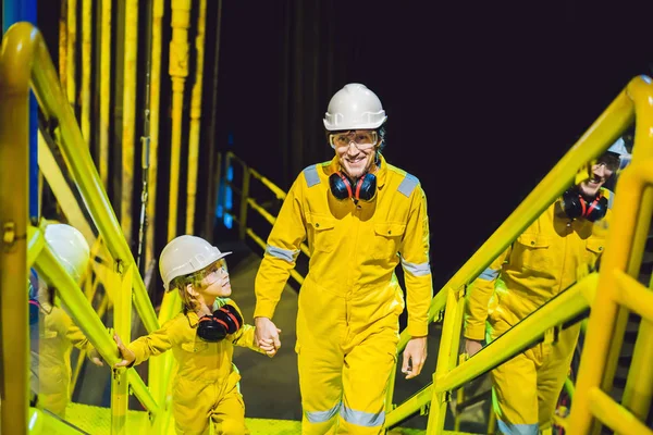 Joven y un niño pequeño están ambos en un uniforme de trabajo amarillo, gafas, y casco en un entorno industrial, Plataforma de petróleo o planta de gas licuado — Foto de Stock