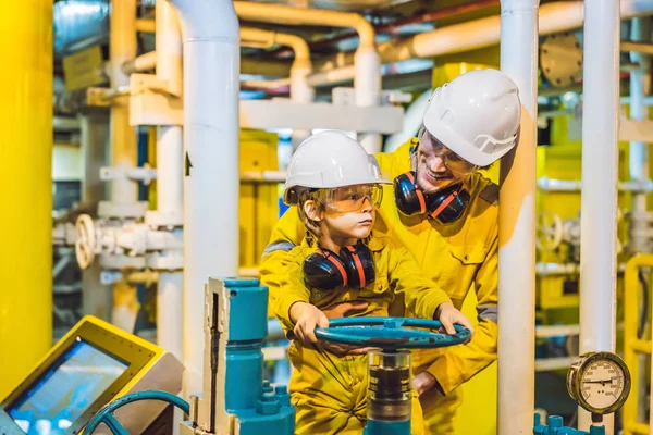 Joven y un niño pequeño están ambos en un uniforme de trabajo amarillo, gafas, y casco en un entorno industrial, Plataforma de petróleo o planta de gas licuado — Foto de Stock