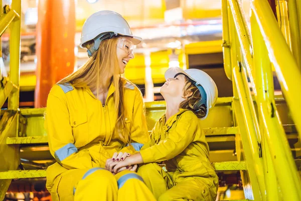 Giovane donna e un bambino sono entrambi in uniforme da lavoro gialla, occhiali e casco in un ambiente industriale, piattaforma petrolifera o impianto di gas liquefatto — Foto Stock