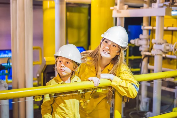 Mladá žena a malý chlapec jsou oba ve žluté pracovní uniformě, brýlích a helmě v průmyslovém prostředí, ropné plošině nebo zkapalněné plynové elektrárně — Stock fotografie