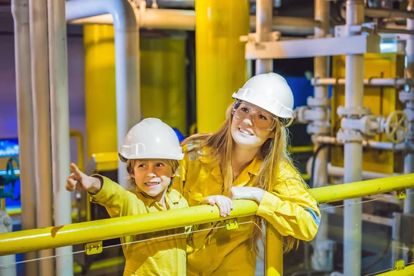 Mujer joven y un niño pequeño están ambos en un uniforme de trabajo amarillo, gafas y casco en un entorno industrial, plataforma petrolera o planta de gas licuado — Foto de Stock