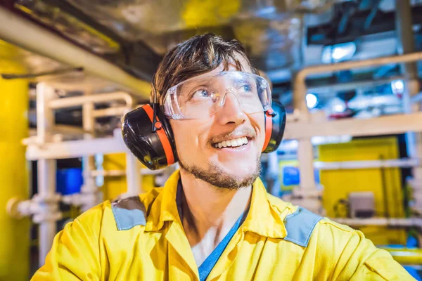 Joven en uniforme de trabajo amarillo, gafas y casco en ambiente industrial, plataforma petrolera o planta de gas licuado — Foto de Stock