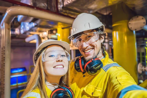 Muž a žena ve žluté pracovní uniformě, brýle a helmici v průmyslovém prostředí, ropná plošina nebo zařízení na zkapalněný plyn — Stock fotografie