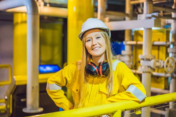 Mujer joven en uniforme de trabajo amarillo, gafas y casco en ambiente industrial, plataforma petrolera o planta de gas licuado — Foto de Stock