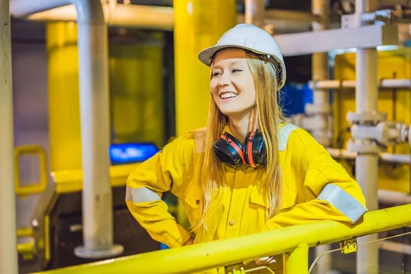 Mujer joven en uniforme de trabajo amarillo, gafas y casco en ambiente industrial, plataforma petrolera o planta de gas licuado — Foto de Stock