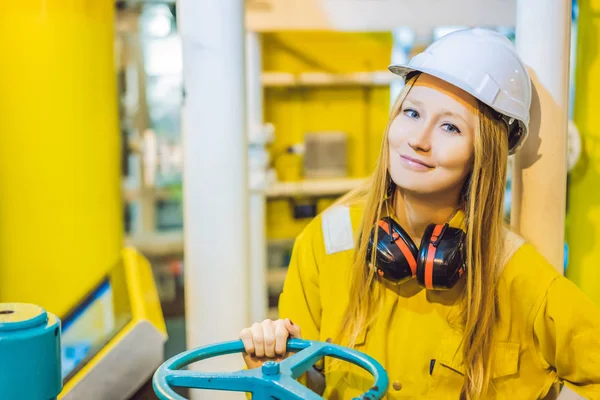 Mujer joven en uniforme de trabajo amarillo, gafas y casco en ambiente industrial, plataforma petrolera o planta de gas licuado — Foto de Stock