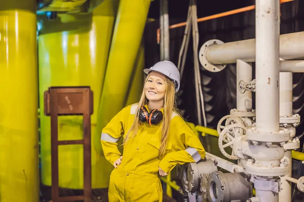 Mujer joven en uniforme de trabajo amarillo, gafas y casco en ambiente industrial, plataforma petrolera o planta de gas licuado — Foto de Stock