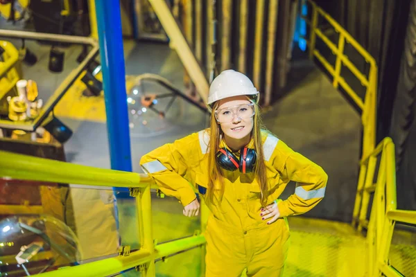 Mujer joven en uniforme de trabajo amarillo, gafas y casco en ambiente industrial, plataforma petrolera o planta de gas licuado — Foto de Stock