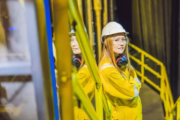 Mujer joven en uniforme de trabajo amarillo, gafas y casco en ambiente industrial, plataforma petrolera o planta de gas licuado — Foto de Stock