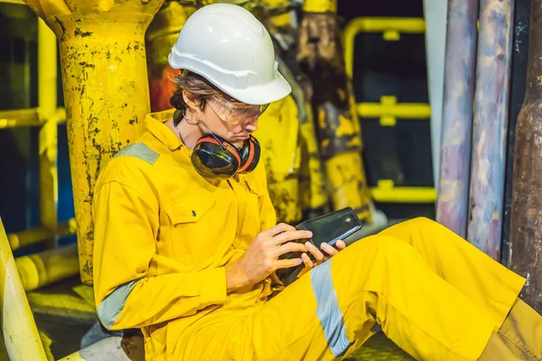 Mladý muž ve žluté pracovní uniformě, brýlích a helmě v průmyslovém prostředí, olejové plošině nebo továrně na zkapalněný plyn hledí do prázdné peněženky. Nevyplácet plat — Stock fotografie