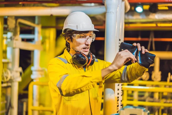 Giovane in uniforme da lavoro gialla, occhiali e casco in ambiente industriale, piattaforma petrolifera o impianto di gas liquefatto guardando nel suo portafoglio vuoto. Non pagare lo stipendio — Foto Stock