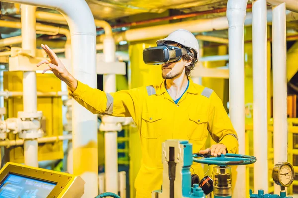 Mujer joven en uniforme de trabajo amarillo, gafas y casco utiliza gafas de realidad virtual en ambiente industrial, plataforma petrolera o planta de gas licuado — Foto de Stock