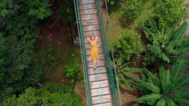 Genç bir kadının havadan çekilmiş fotoğrafı, ormanların üzerindeki asma köprüye uzanıyor. Güney Doğu Asya konseptine seyahat