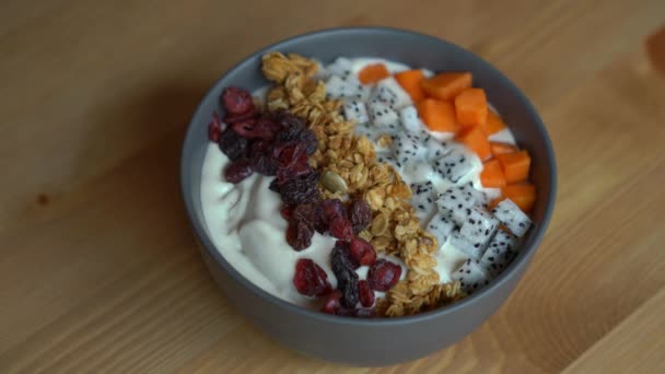 Closeup shot of a process of making a smoothie bowl with papaya, dragon fruit, granola, dried cherry, and pumpkin seeds — Stock Video