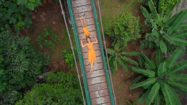 Aerial shot of a young woman and her little son laying on a suspension bridge over the jungles. Travel to South East Asia concept — Stock Video