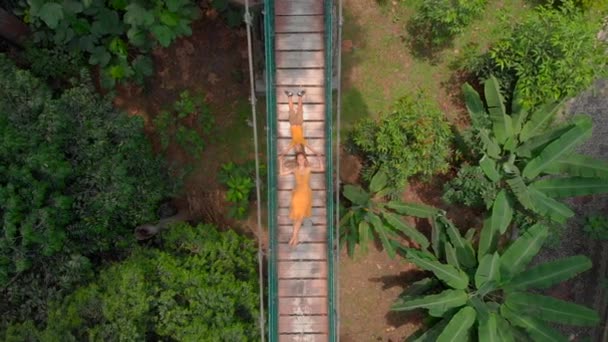 Aerial shot of a young woman and her little son laying on a suspension bridge over the jungles. Travel to South East Asia concept — Stock Video