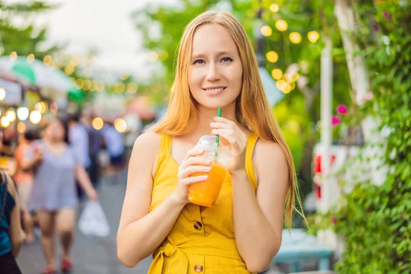 Жінка п'є апельсиновий сік на азіатському ринку. — стокове фото