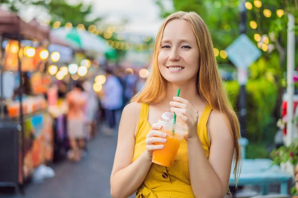 Женщина пьет апельсиновый сок на азиатском рынке — стоковое фото