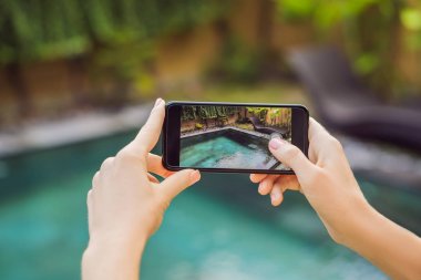 Oteldeki havuzun arka planında el ele tutuşan telefon. Ekrandaki fotoğraf makinesi. Kapat elini akıllı telefon yaz tatilinin fotoğrafını çek.