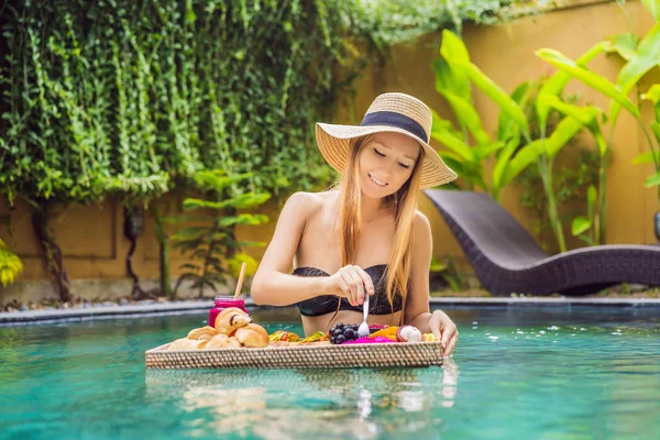 Breakfast tray in swimming pool, floating breakfast in luxury hotel. Girl relaxing in the pool drinking smoothies and eating fruit plate, smoothie bowl by the hotel pool. Exotic summer diet. Tropical