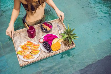 Yüzme havuzunda kahvaltı tepsisi, lüks otelde yüzen kahvaltı. Havuzda dinlenen kız smoothies içme ve meyve tabağı, otel havuzu yanında smoothie kase yemek. Egzotik yaz diyeti. Tropikal