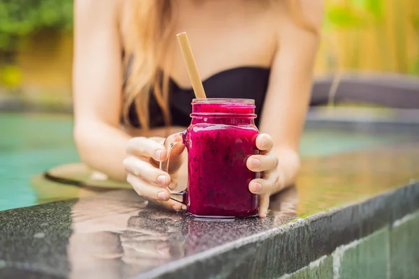 Young woman drinking Dragon fruit smoothies on the background of the pool. Fruit smoothie - healthy eating concept. Close up of detox smoothie with Dragon fruit — Stock Photo, Image