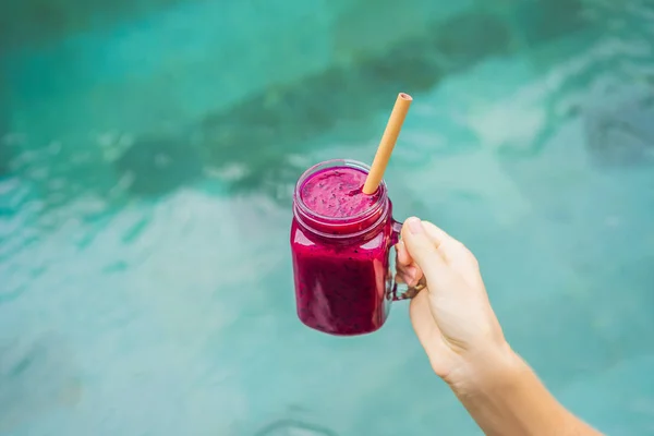 Young woman drinking Dragon fruit smoothies on the background of the pool. Fruit smoothie - healthy eating concept. Close up of detox smoothie with Dragon fruit