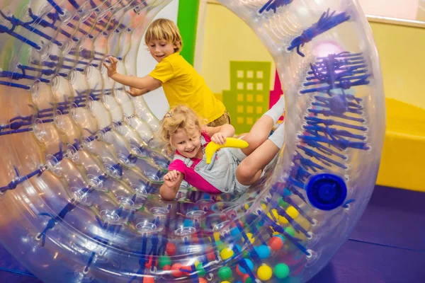 Симпатичный мальчик и девочка играют в Zorb катящийся пластиковый цилиндр кольцо с отверстием в середине, в помещении — стоковое фото