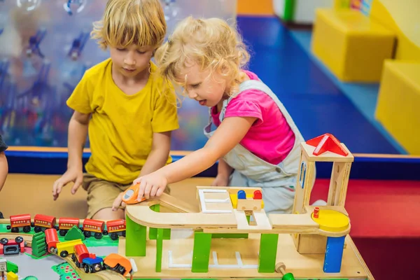 Niños jugando con tren de madera. Niño y bebé juegan con bloques, trenes y coches. Juguetes educativos para niños de preescolar y jardín de infantes. Niño y niña construyen ferrocarril de juguete en casa o guardería — Foto de Stock