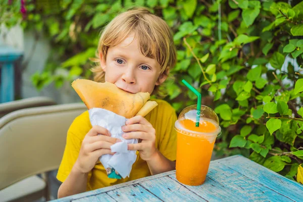 Dulce niño caucásico, comiendo panqueques y bebiendo jugo de naranja — Foto de Stock