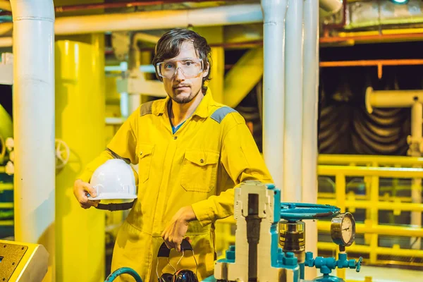 Joven en uniforme de trabajo amarillo, gafas y casco en ambiente industrial, plataforma petrolera o planta de gas licuado — Foto de Stock