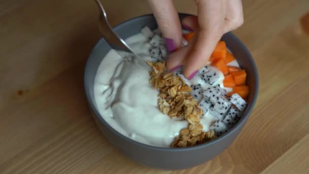 Closeup shot of a process of making a smoothie bowl with papaya, dragon fruit, granola, dried cherry, and pumpkin seeds — Stock Video