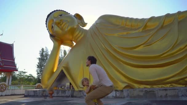 Slowmotion постріл молодого чоловіка і його маленького сина веселяться перед статуєю лежачого Будди на острові Пхукет. Travell в Таїланді концепція — стокове відео