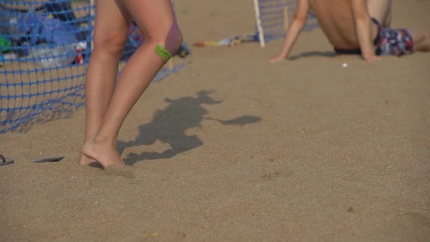 Piernas de una mujer y su sombra corporal jugando voleibol en una playa — Vídeo de stock