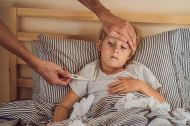 Termometreli hasta çocuk yatakta yatıyor ve baba el ateş alıyor. baba termometresi olan hasta oğlunun sıcaklığını kontrol ediyor. Yatakta ateşi ve hastalığı olan hasta çocuk