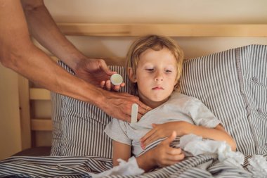 Sick boy with thermometer laying in bed and father hand taking temperature. father checking temperature of her sick son who has thermometer. Sick child with fever and illness in bed clipart