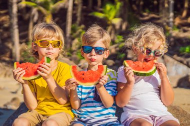 Çocuklar güneş gözlüğü ile plajda karpuz yemek