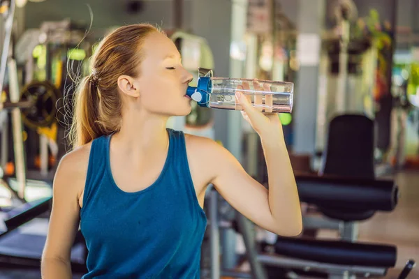 Mujer atlética joven bebiendo agua en el gimnasio — Foto de Stock