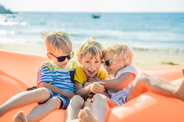I bambini siedono su un divano gonfiabile contro il mare e si divertono — Foto Stock