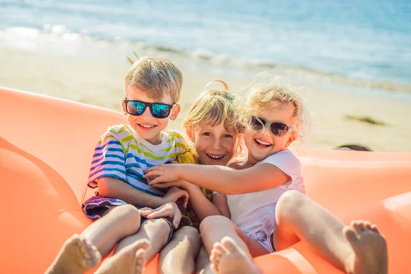 I bambini siedono su un divano gonfiabile contro il mare e si divertono — Foto Stock